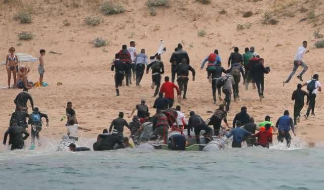 Imigrantes chegam a praia na Espanha, observados por turistas